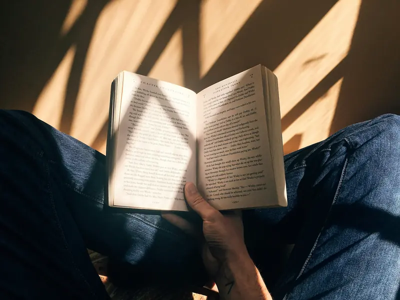 An open paperback held in a reader’s lap in warm afternoon light